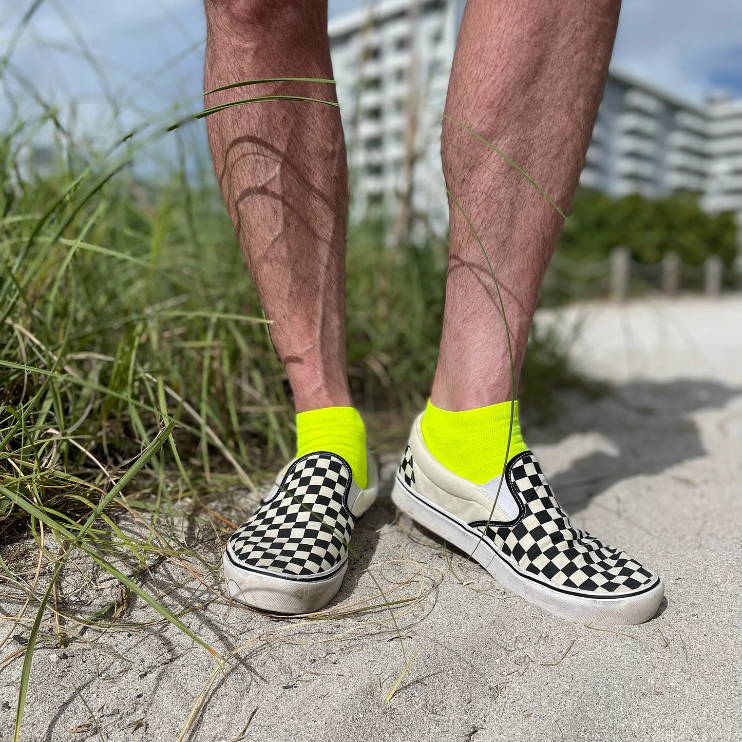 man standing on a beach wearing checkerboard Vans and bright yellow DeFeet All Day cycling socks with a 1" cuff