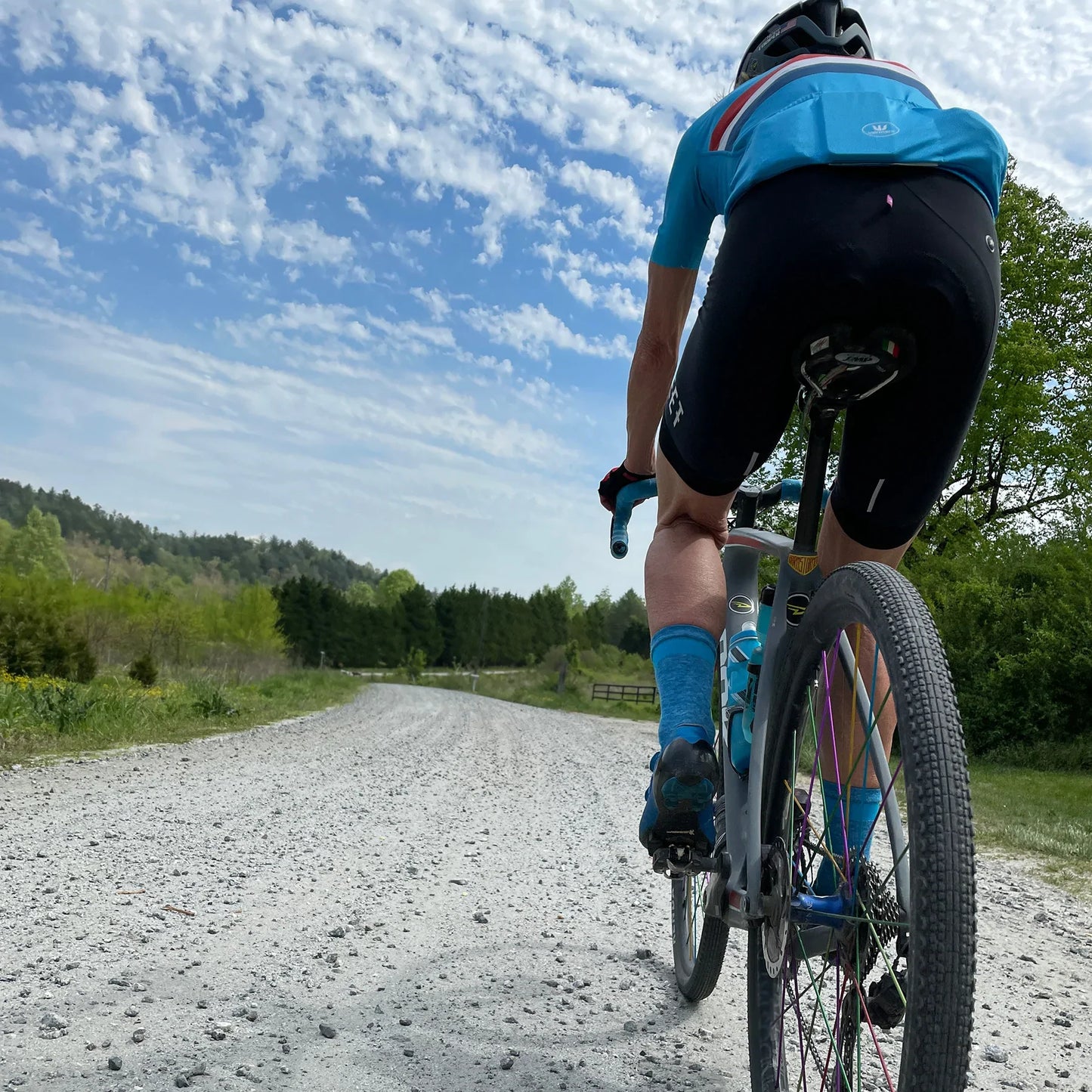 white female cyclist riding on a gravel road wearing blue cycling socks