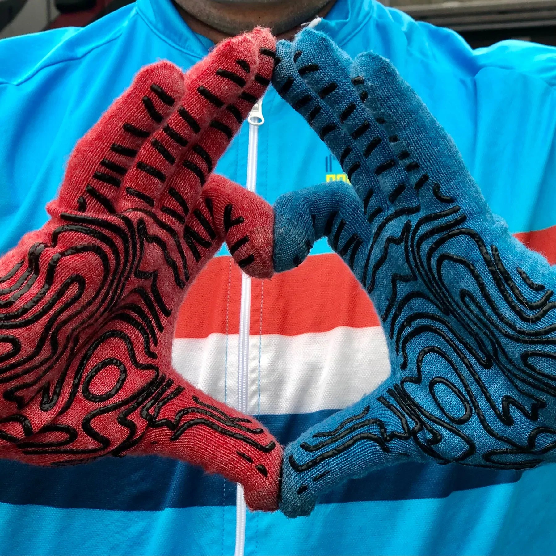 man wearing one red and one blue Merino wool DeFeet cycling glove with topo black grip lines on the palm